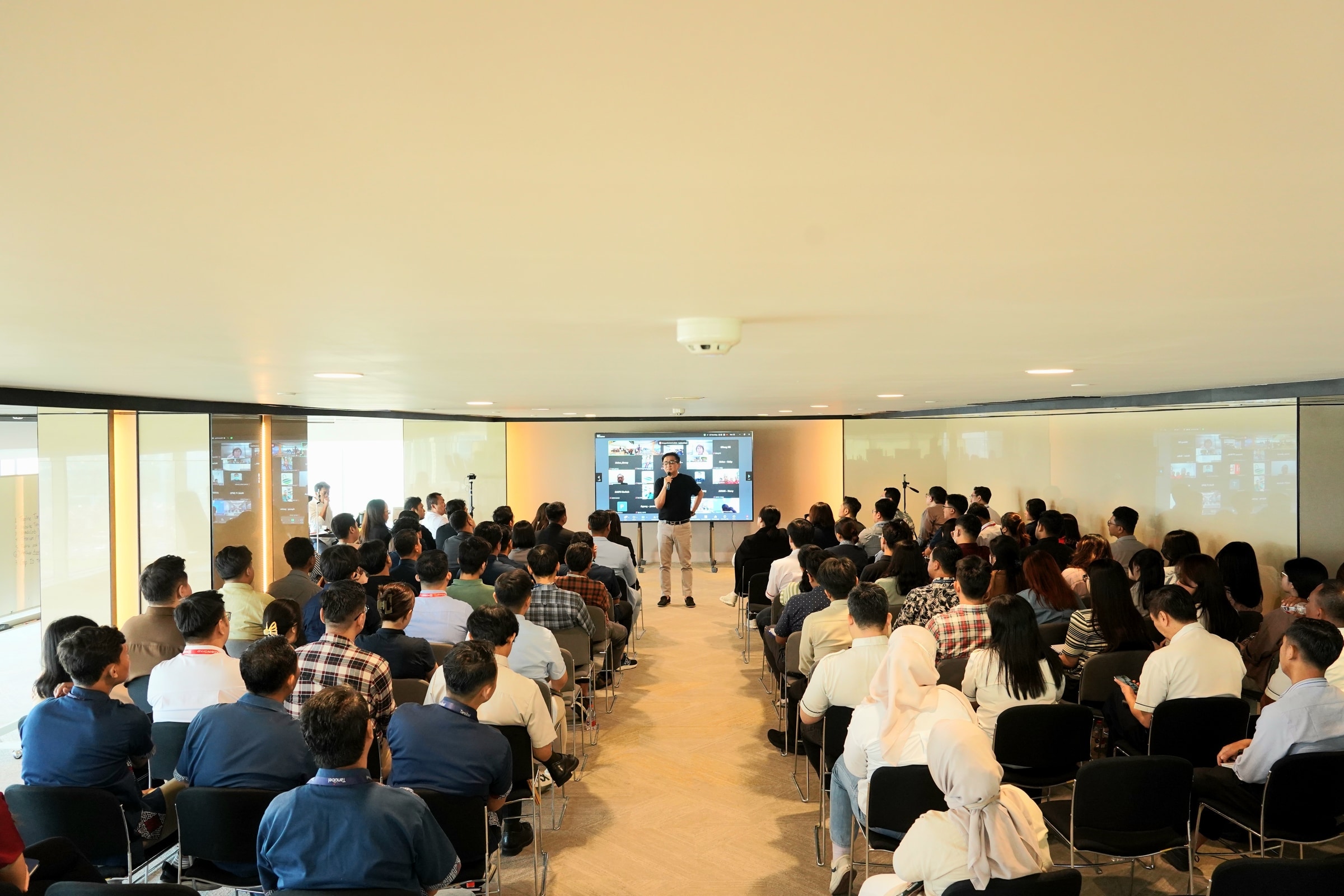 Wide view of a seated corporate audience with a presenter in the distance.