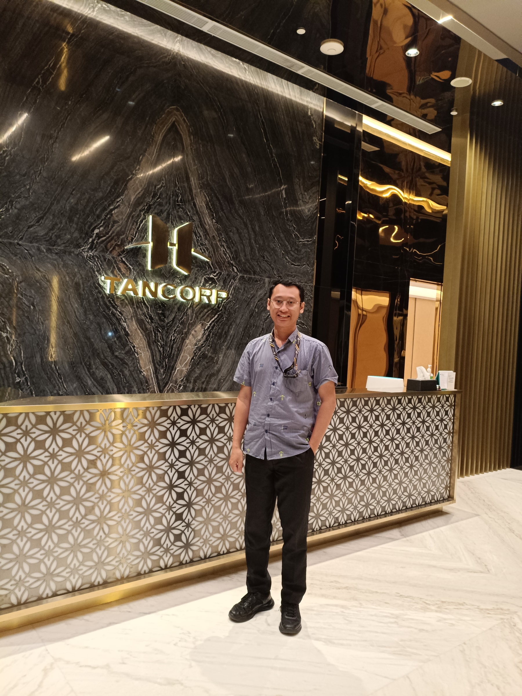 Olisiang standing in front of the Tancorp lobby wall.