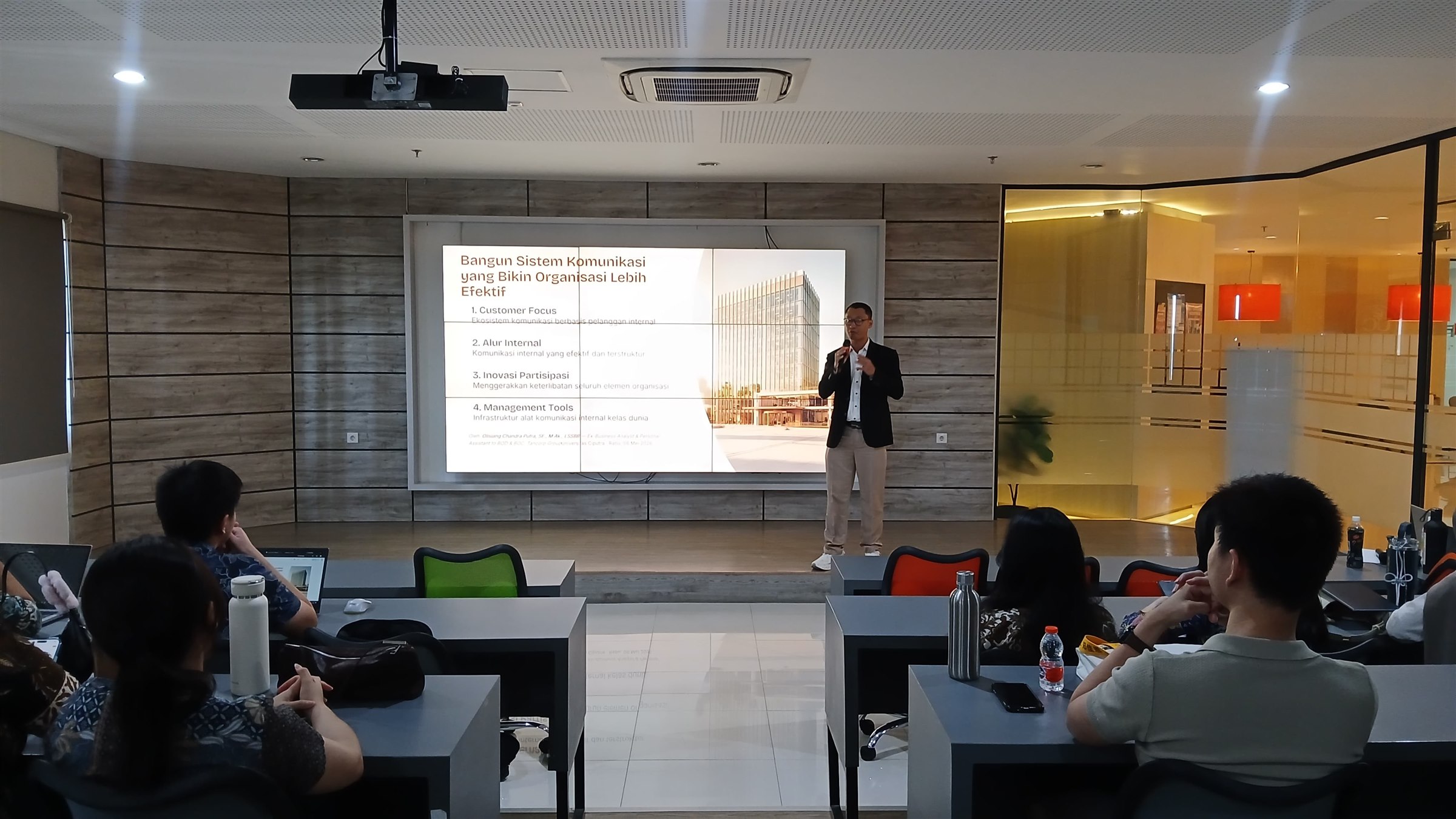 Olisiang presenting beside a projected slide at Universitas Ciputra.
